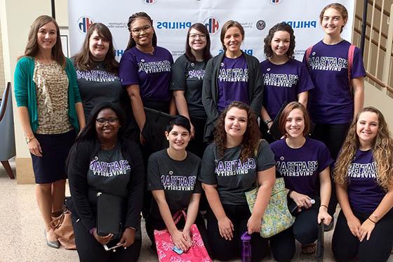 Photo of the Chatham 室合唱团, wearing purple Chatham University t-shirts, posing together for a photo with the choir director